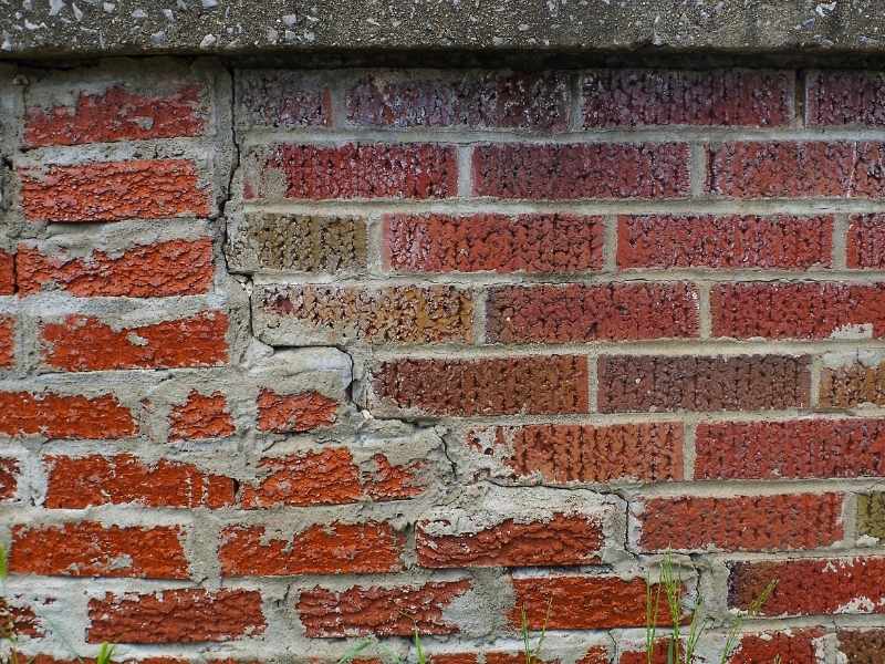 Close-up of a residential brick wall with stair-step cracks and deteriorating mortar, indicating the need for professional brick repair.
