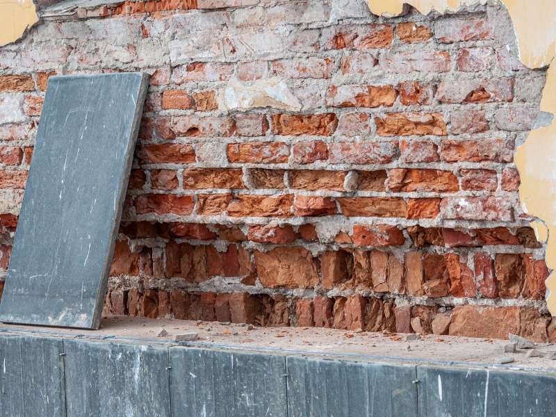 Masonry contractor repairing cracked brick joints and deteriorated mortar before repainting a residential brick exterior.
